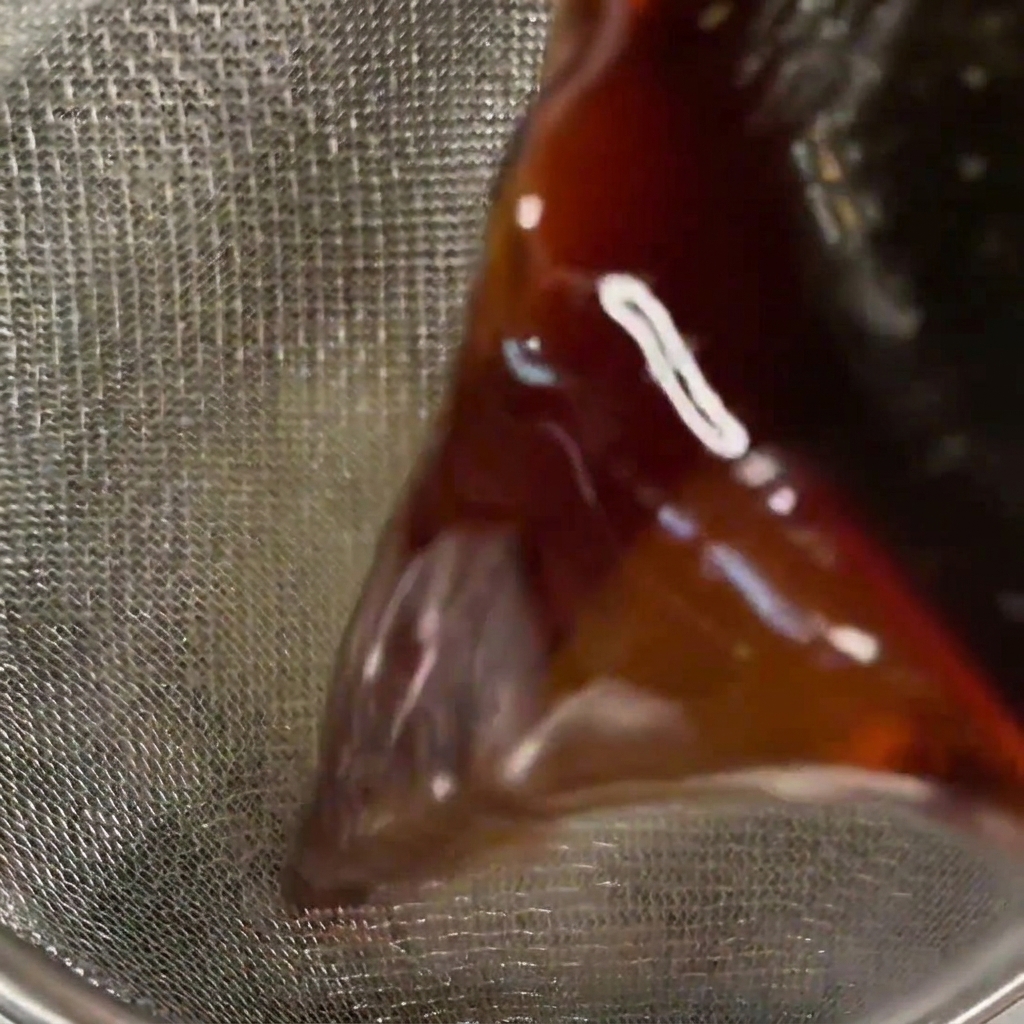 Salsa scura versata attraverso un colino a maglia fine.