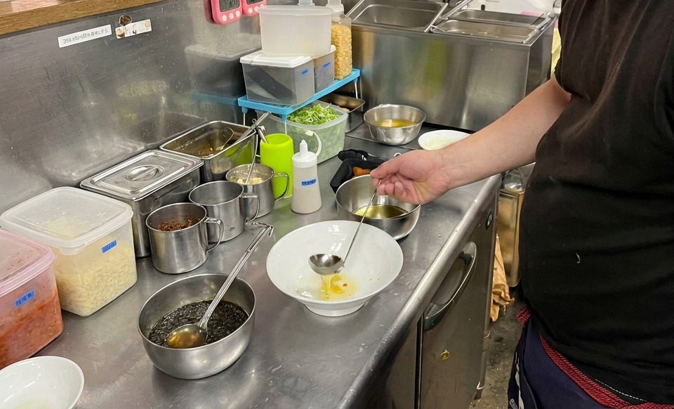 Un mestolo che versa olio dorato sul fondo di una ciotola bianca.