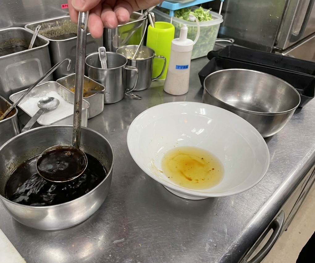 Salsa di soia scura versata nella ciotola sopra lolio chiaro.