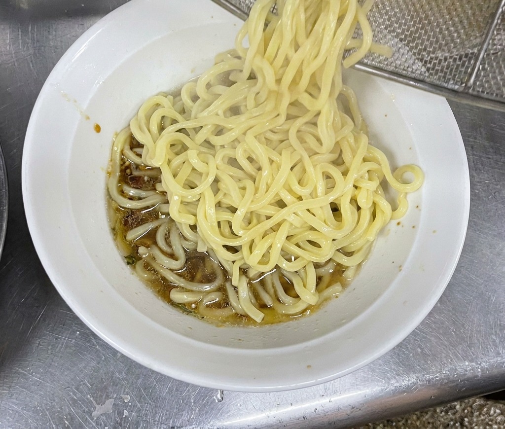 Noodles fumanti versati nella ciotola con il condimento sul fondo.