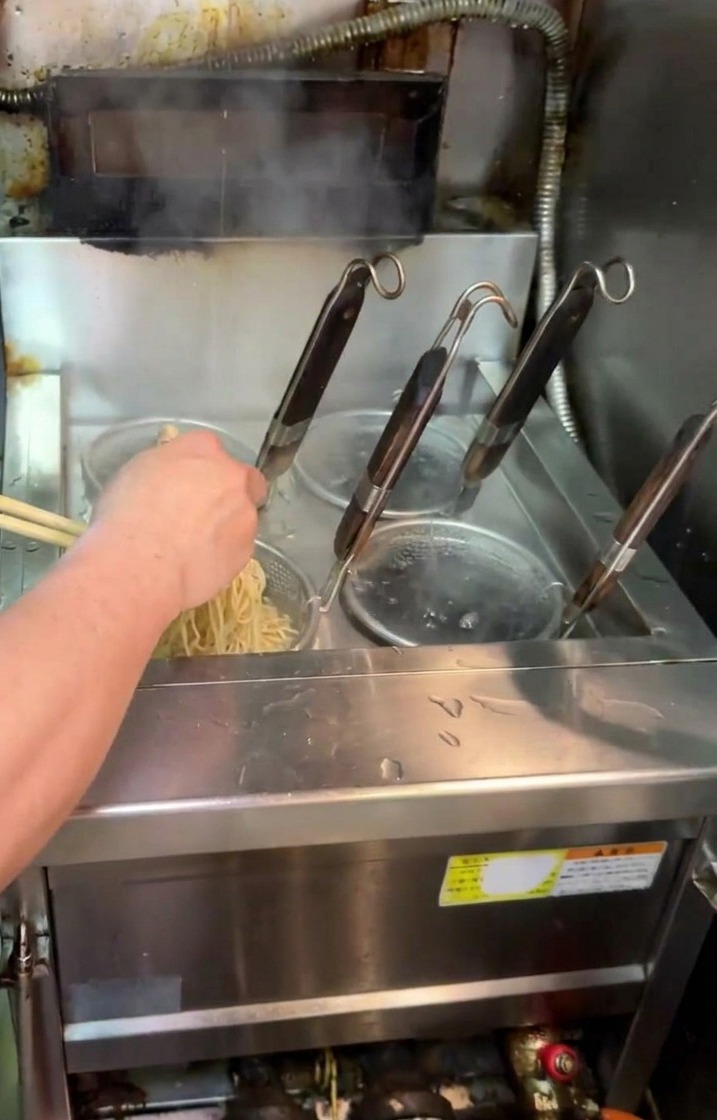 Un cuoco solleva un colino a rete dallacqua bollente scuotendo i noodle per scolarli.