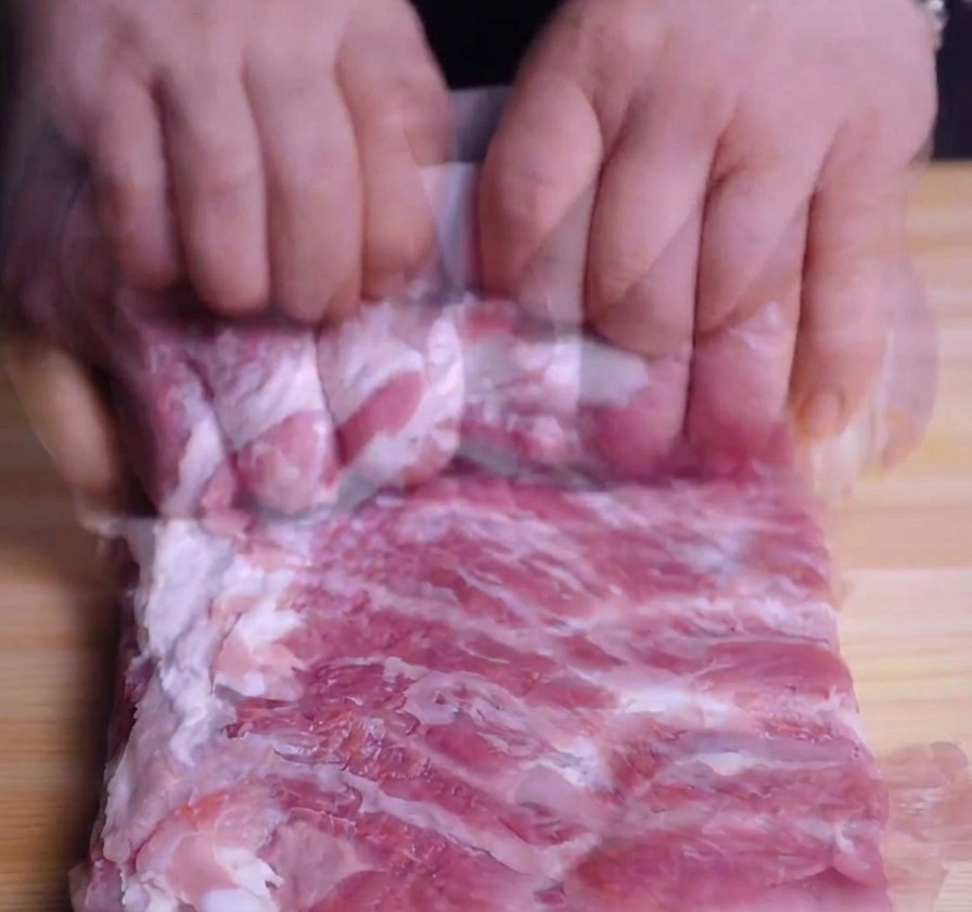 Mani che arrotolano strettamente una lastra di pancetta di maiale per formare un cilindro.