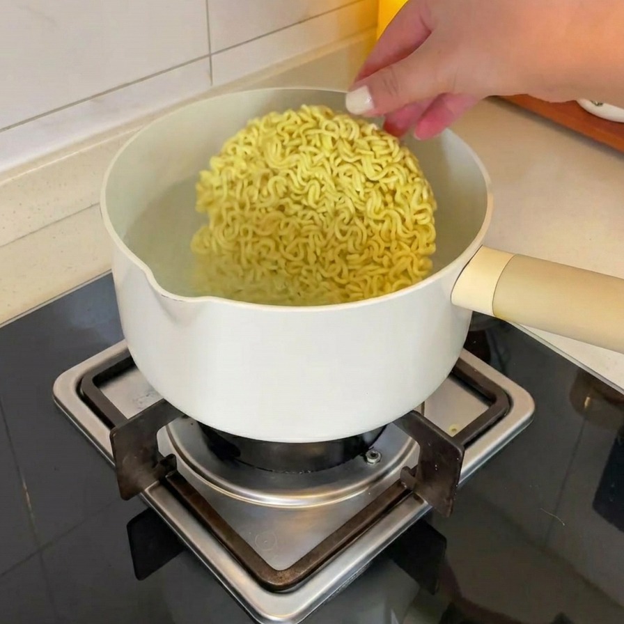 Una mano che mette un panetto di noodle istantanei secchi in una pentola di acqua bollente.