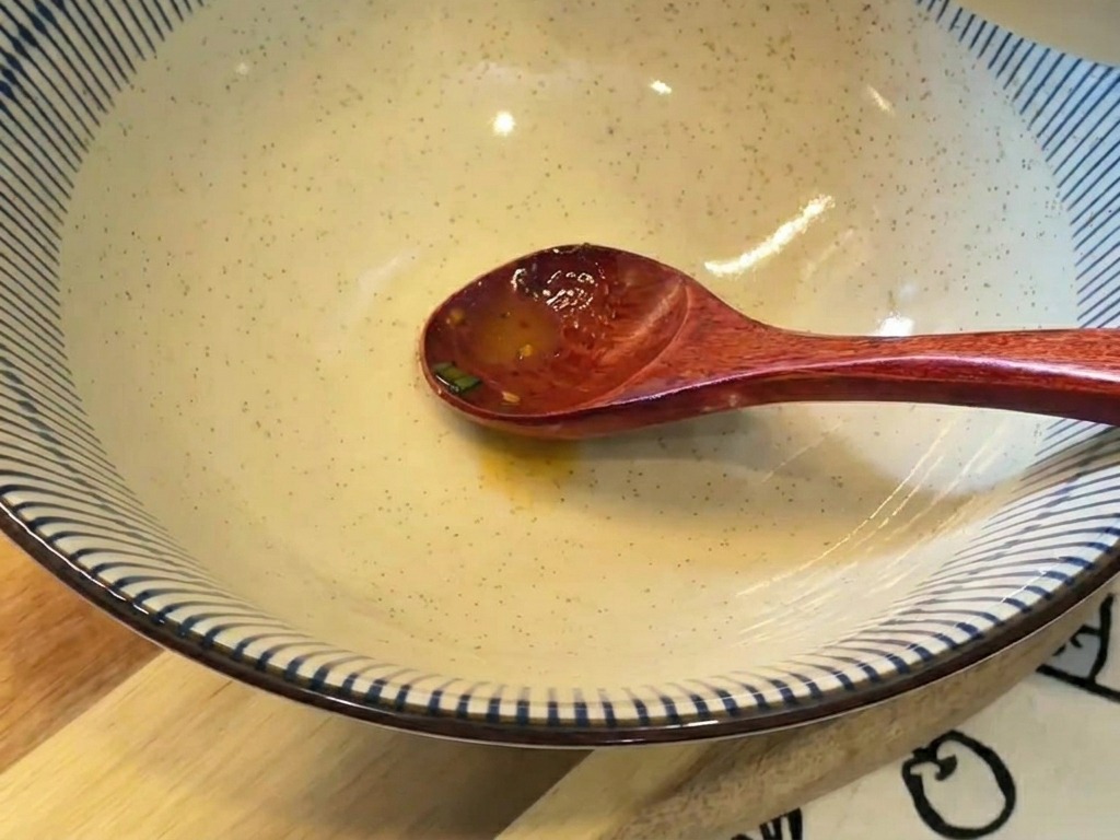 Brodo cremoso arancione versato da una ciotolina in una grande ciotola in ceramica a strisce bianche e blu.