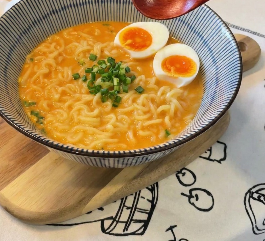 Ciotola di ramen guarnita con uova e una manciata di cipollotti freschi al centro.