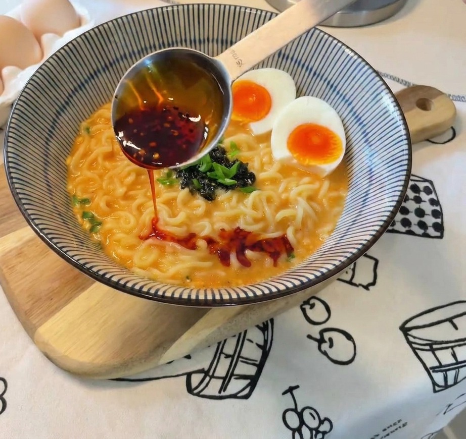Olio al peperoncino rosso versato da un cucchiaio dosatore su una ciotola finita di ramen.