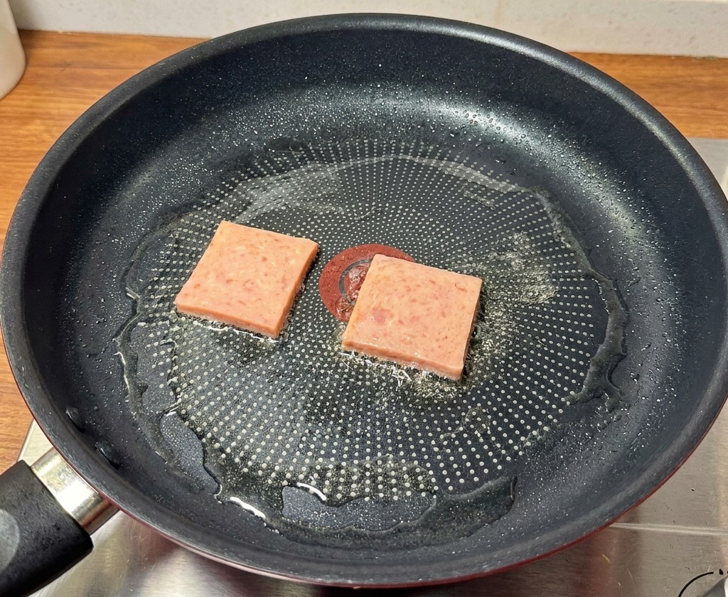 Fette di carne in scatola che sfrigolano in una padella antiaderente fino a diventare dorate e croccanti.