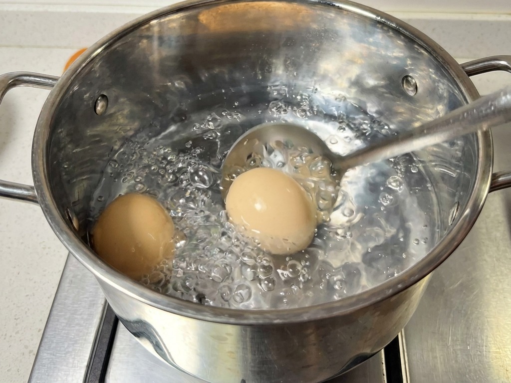 Una schiumarola solleva due uova sode da una pentola dacqua bollente.