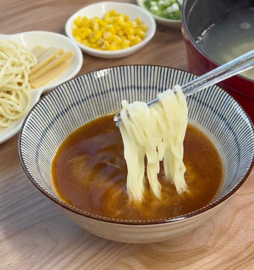 Noodle cotti aggiunti e disposti con le bacchette in una ciotola piena di brodo al miso scuro.