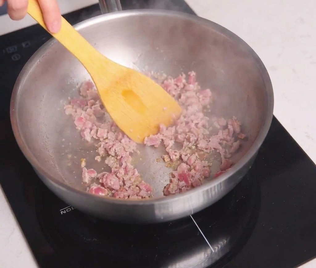 Carne macinata sgranata e saltata in una padella dacciaio con una spatola gialla fino a doratura.