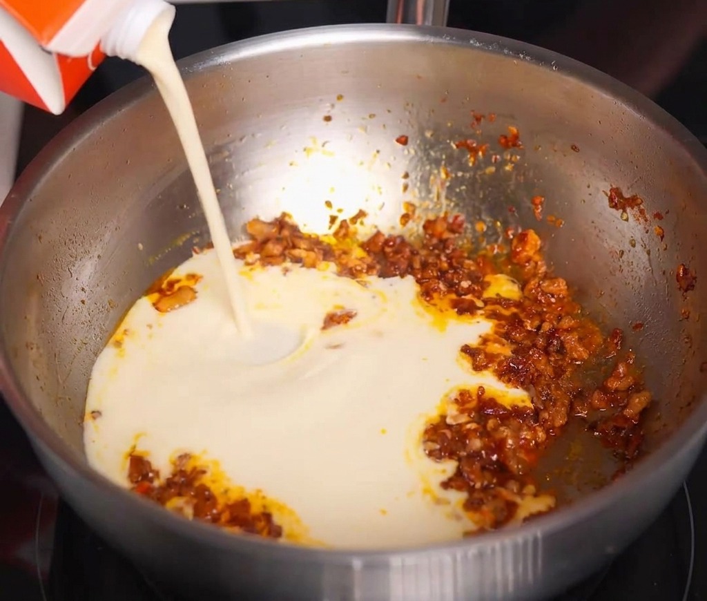 Latte di soia bianco e cremoso versato da un cartone nella padella con il condimento piccante.