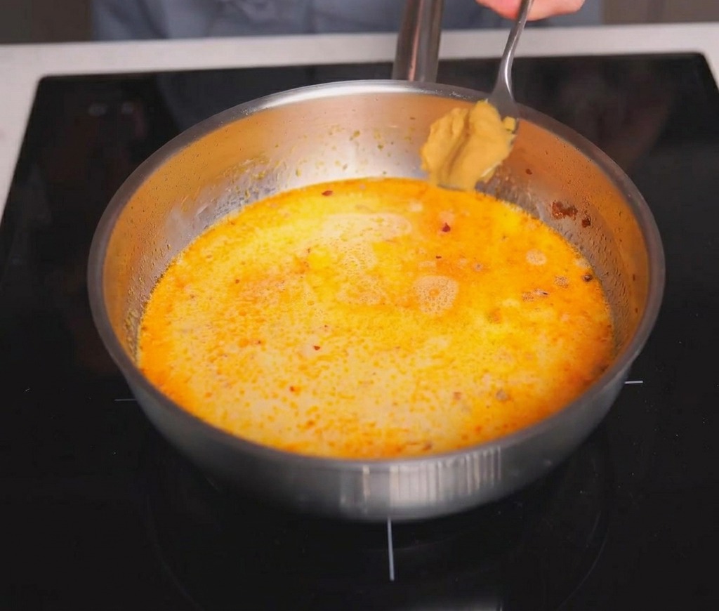 Un cucchiaio di pasta di miso marrone aggiunto al brodo cremoso che sobbolle delicatamente.