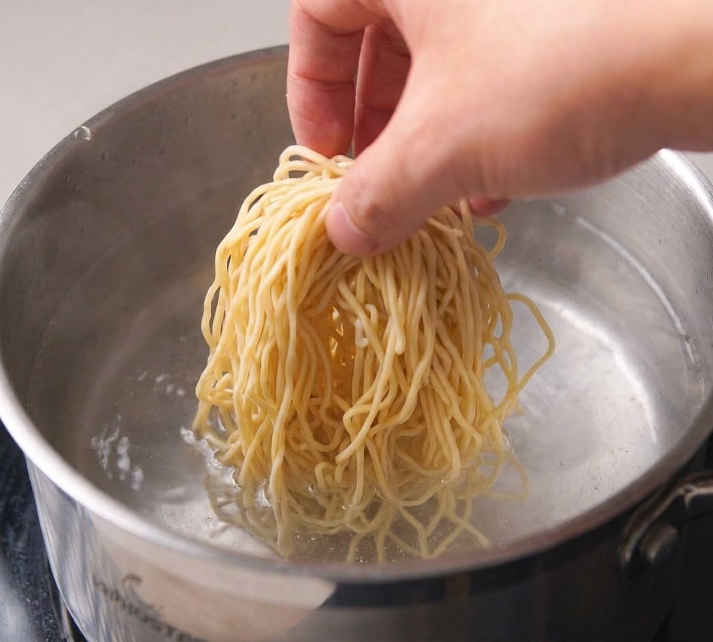 Pentola dacciaio con acqua sul fuoco che inizia a presentare bollicine di ebollizione sul fondo.