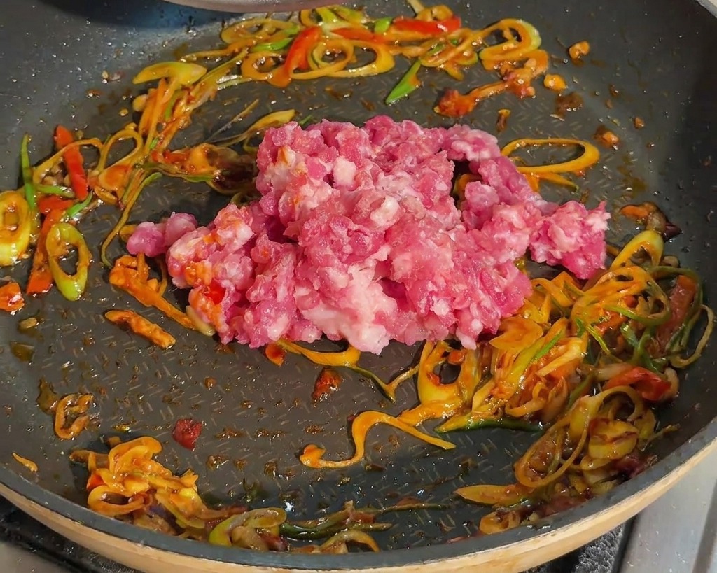 Carne di maiale macinata cruda aggiunta in padella con cipollotti e pasta di fagioli rossa.