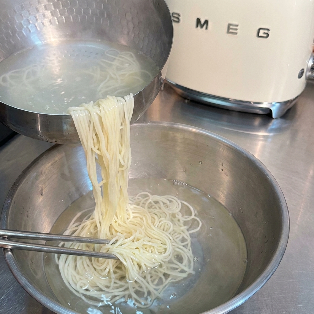 Noodles ramen cotti risciacquati e mossi con bacchette in una ciotola di acqua fredda.