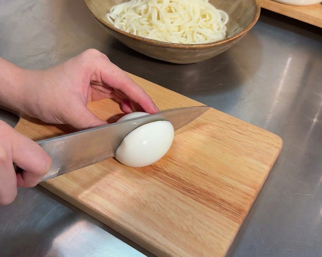 Un coltello affilato taglia a metà un uovo sodo su un tagliere di legno chiaro.