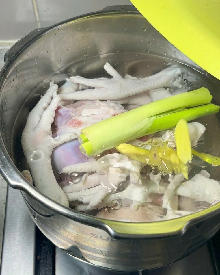 Cipollotti freschi e fette di zenzero appoggiati sopra la carne cruda e lacqua allinterno di una pentola.