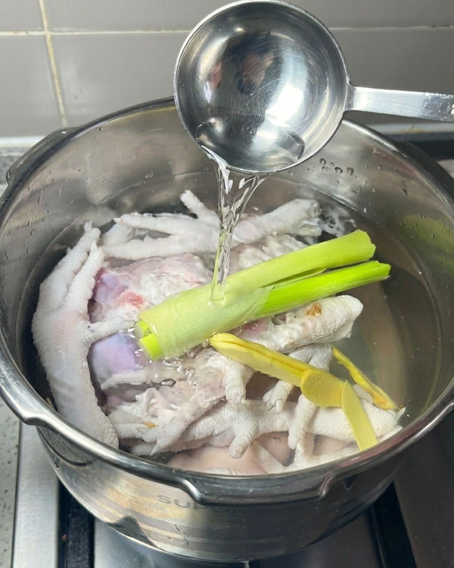 Una pentola a pressione riempita con zampe di gallina, zenzero e cipollotti mentre viene versato del vino bianco da un mestolo.