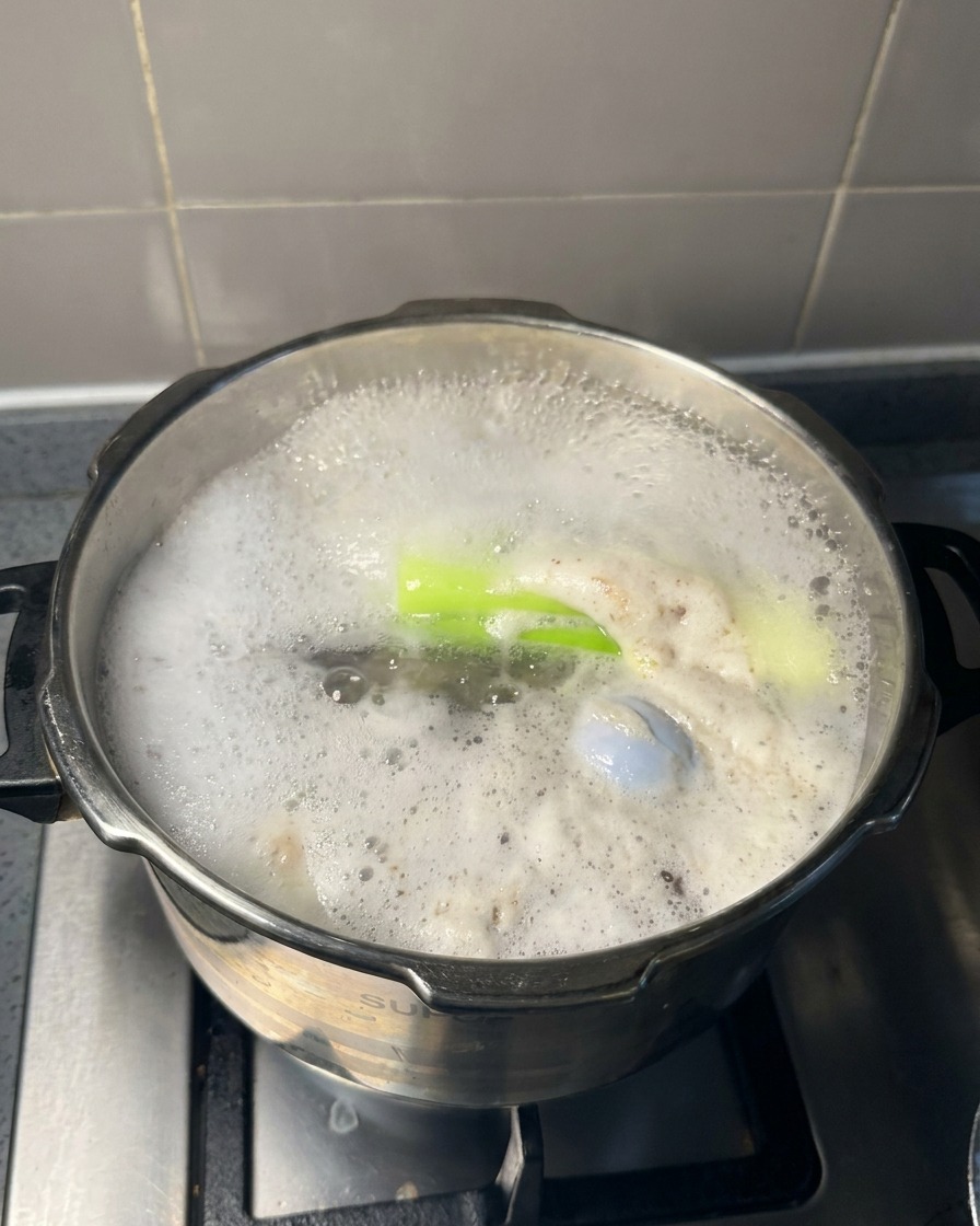 Un grande cucchiaio di metallo solleva schiuma grigia e bolle dalla superficie di un brodo di carne in ebollizione.