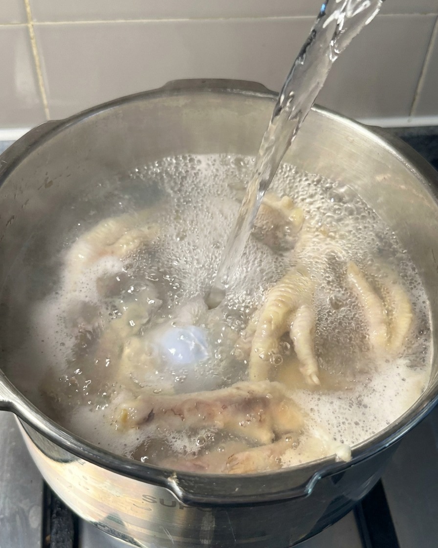 Acqua bollente versata in una pentola contenente zampe di gallina e ossa di maiale parzialmente cotte.