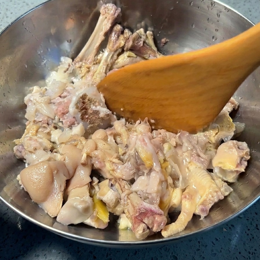 Una spatola di legno preme su piedini di maiale e zampe di gallina cotti per separare carne e pelle dalle ossa.