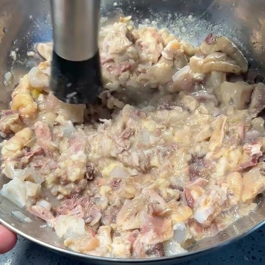 Uno schiacciapatate in metallo riduce la carne di maiale e pollo cotta in una pasta grossolana sul fondo di una ciotola.