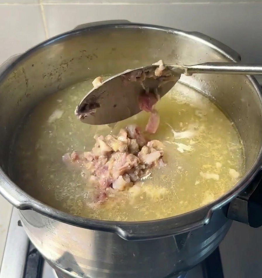 Un grande cucchiaio di metallo fa cadere poltiglia di carne cotta e midollo in una pentola di brodo limpido.