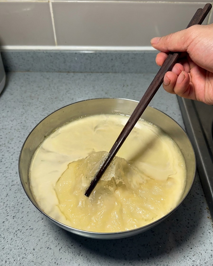 Una mano usa bacchette di legno per rimuovere uno strato sottile di grasso giallo solidificato sopra un brodo freddo e gelatinoso.
