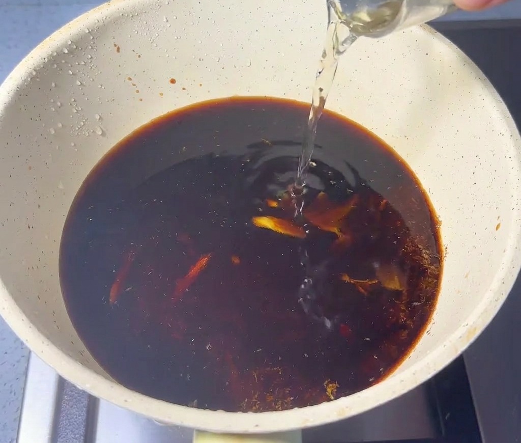 Liquido trasparente versato in un pentolino beige contenente salsa scura e polvere di pesce.