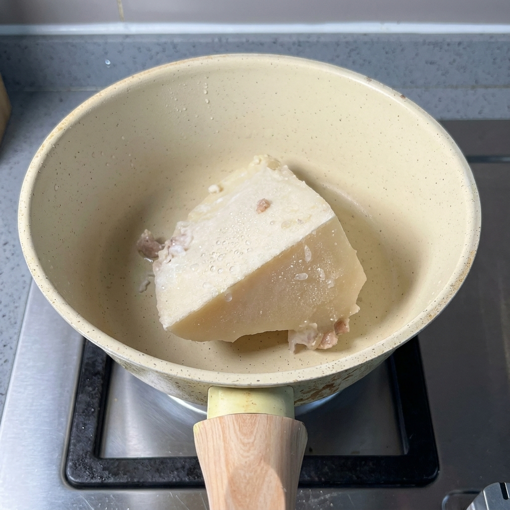 Un blocco di brodo dossa congelato e un cucchiaio di polvere di pesce in un pentolino beige.