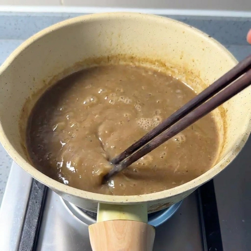 Brodo di maiale denso mescolato con polvere di pesce in un pentolino usando delle bacchette di legno.