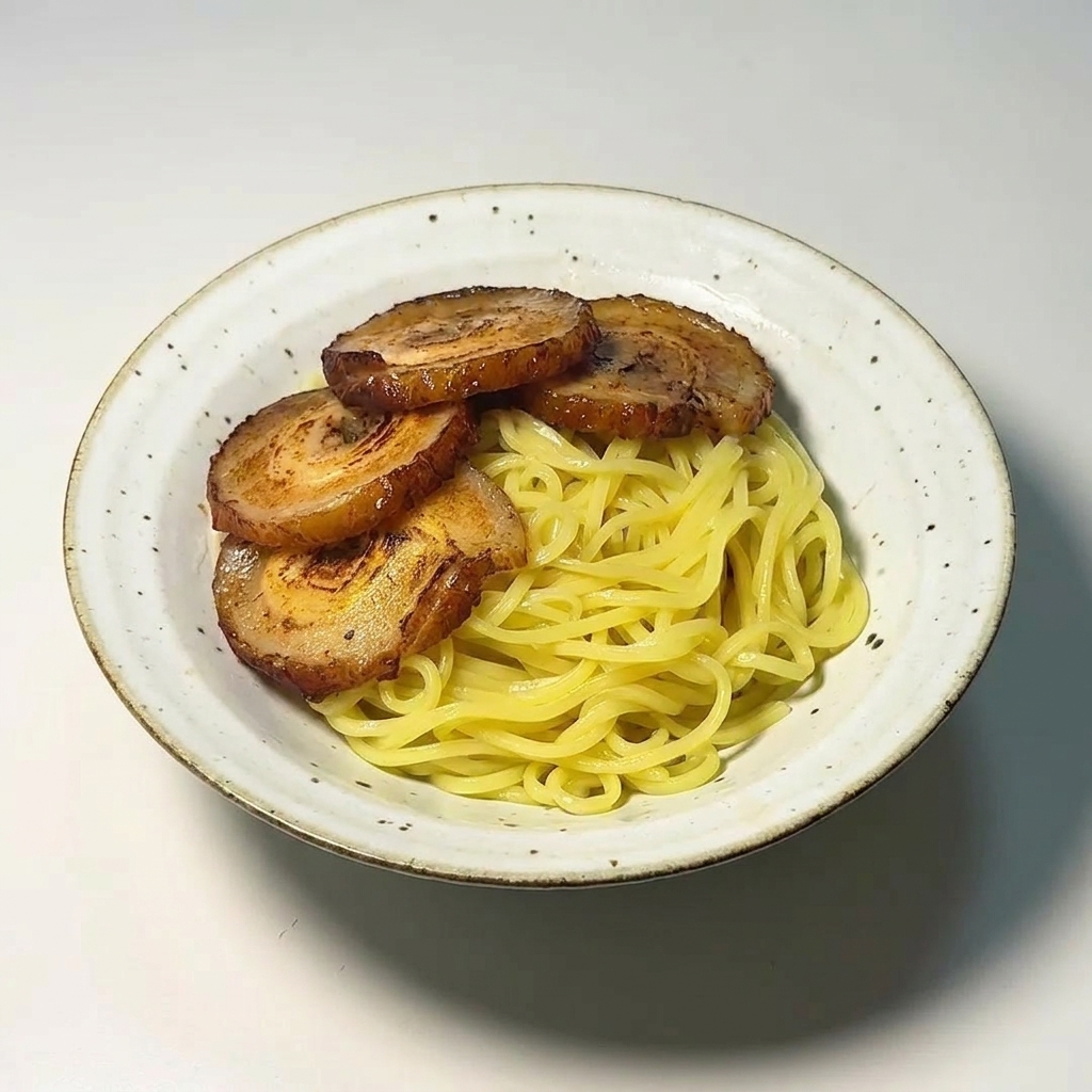 Quattro fette di chashu rosolato disposte ordinatamente su un letto di noodle ramen in una ciotola bianca.