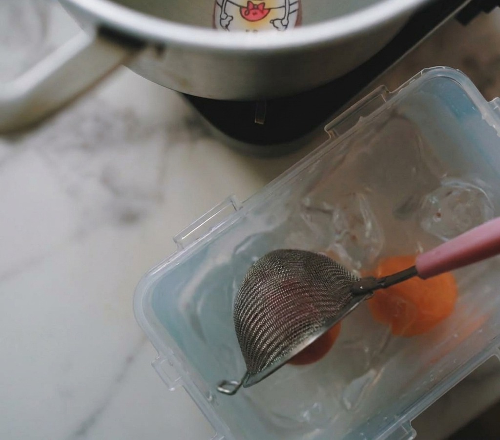 Un colino solleva un uovo sodo da una pentola e lo immerge in un contenitore con ghiaccio e acqua.