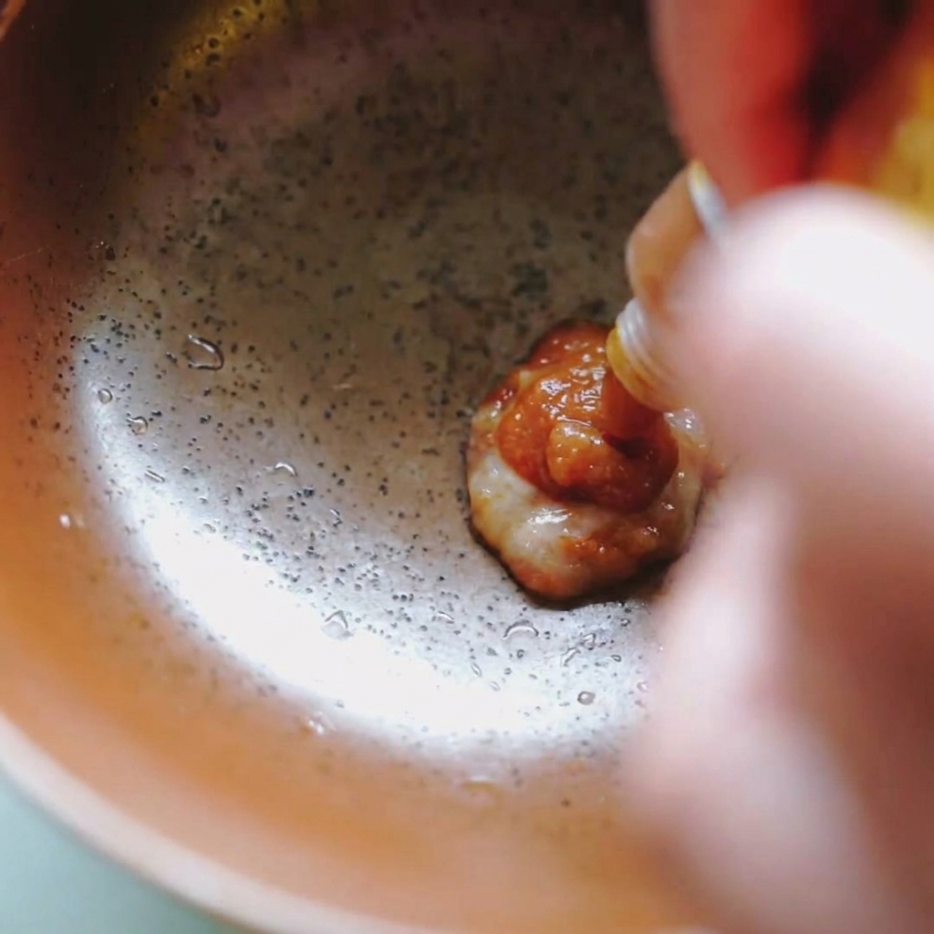 Pasta di miso densa e marrone spremuta da una bustina bianca e gialla in una ciotola di ceramica.
