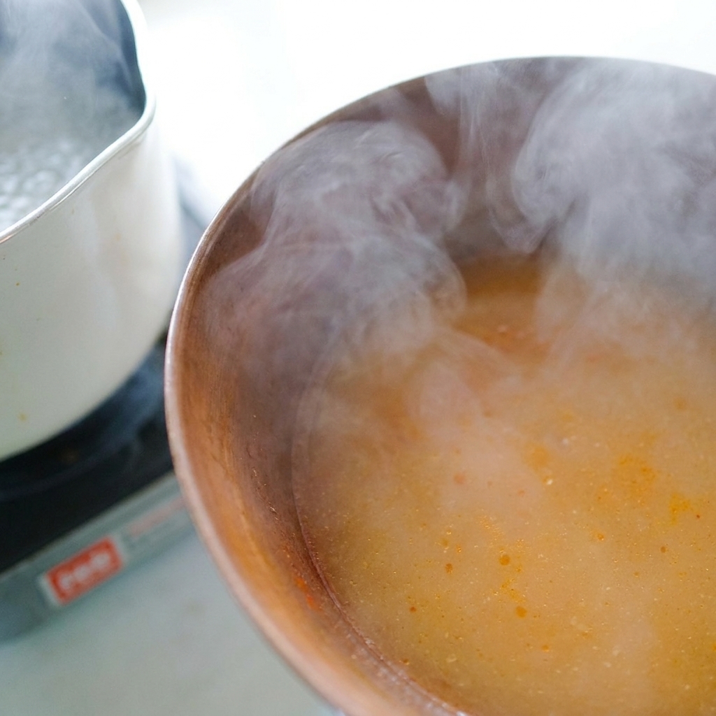 Acqua bollente dei noodles versata con un mestolo in una ciotola con pasta di miso per formare il brodo.