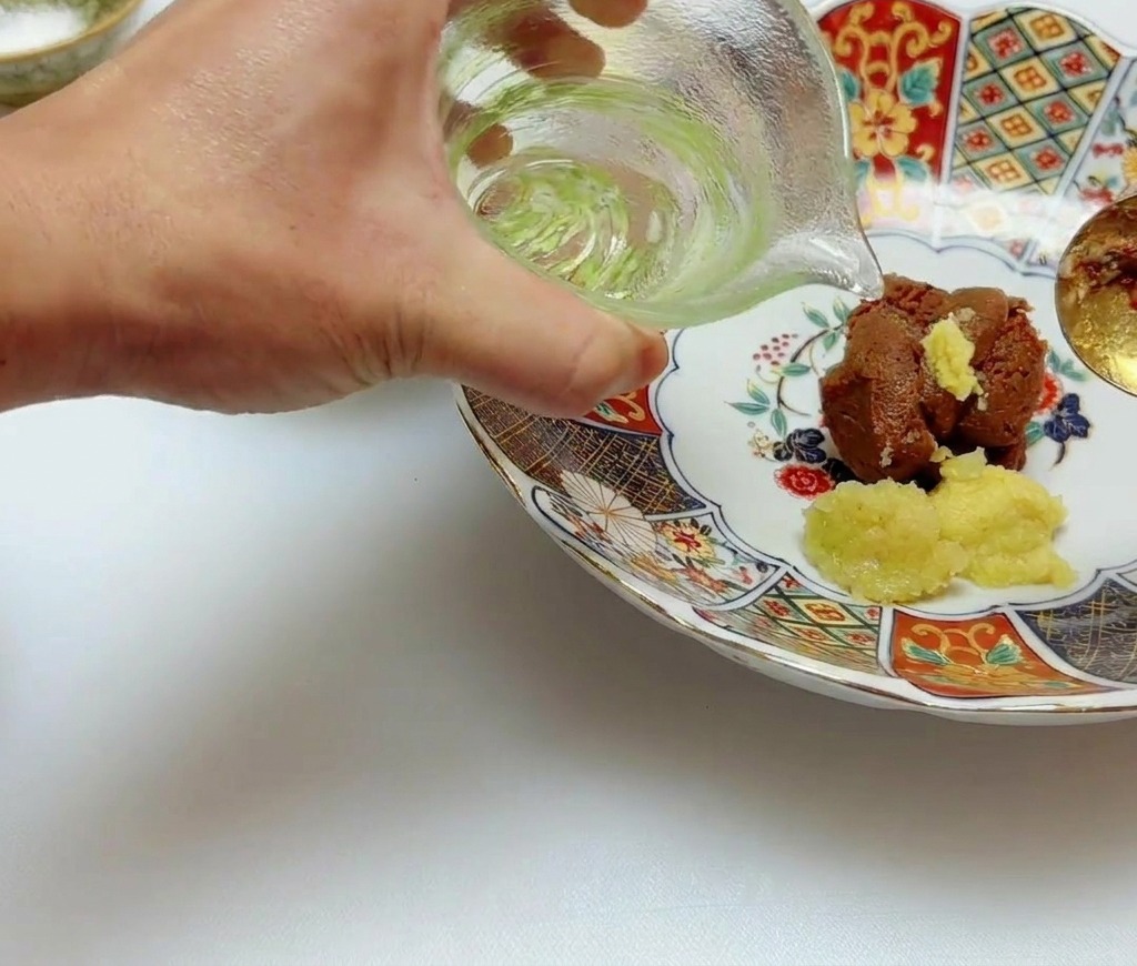 Olio di semi trasparente versato da una caraffa di vetro sul miso e la pasta di zenzero in una ciotola.