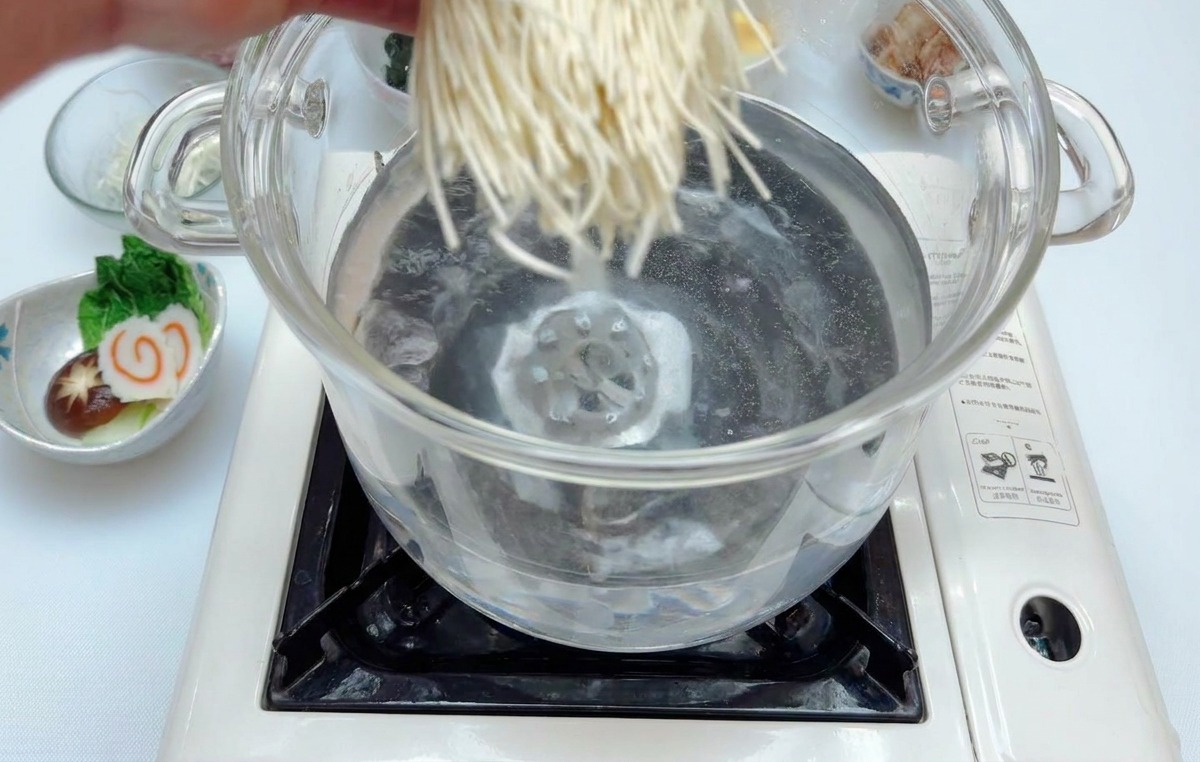Una mano che cala un nido di noodles bianchi sottili in una pentola dacqua bollente su un piano a induzione.