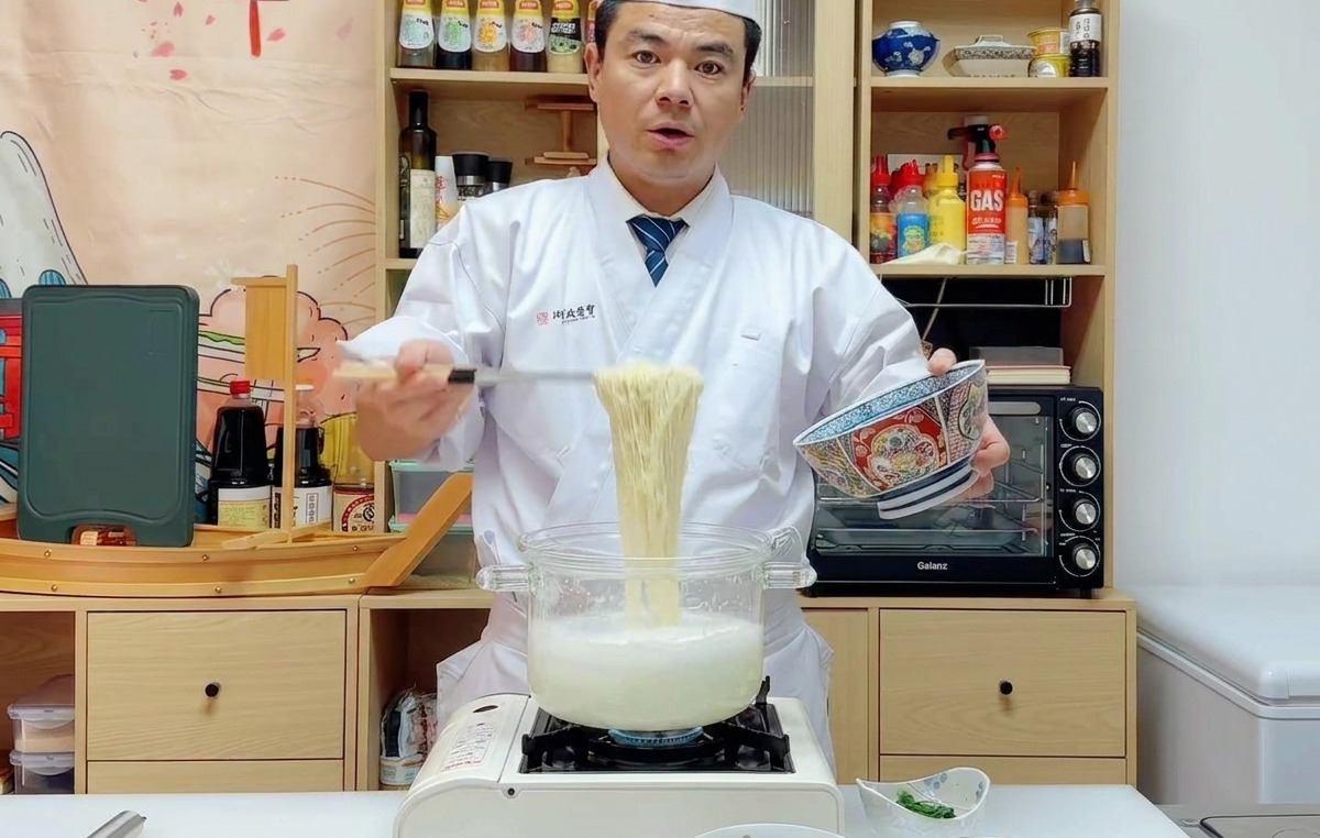 Lo chef Wu solleva i noodles cotti con un colino e li trasferisce in una ciotola blu decorata.