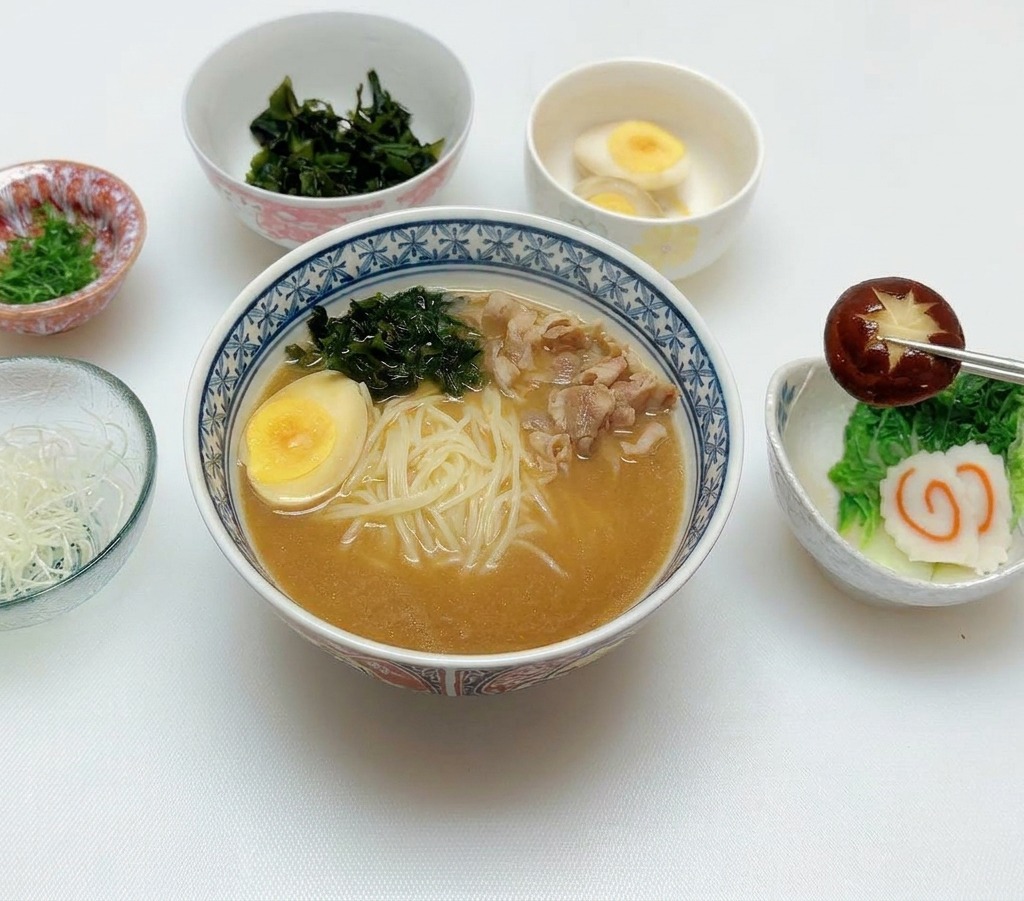 Bacchette che posizionano un fungo shiitake inciso sopra i condimenti di una ciotola di ramen al miso.