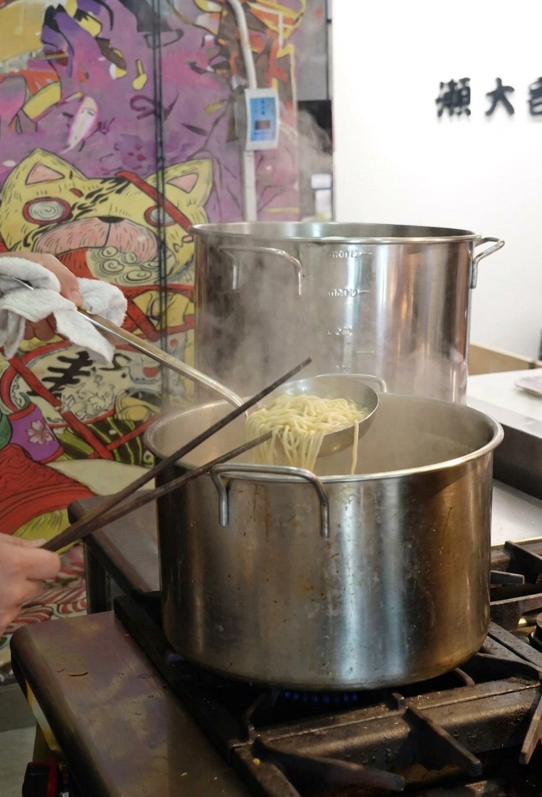 Una persona che usa un colino a rete per sollevare i noodle cotti da una grande pentola di acqua bollente.