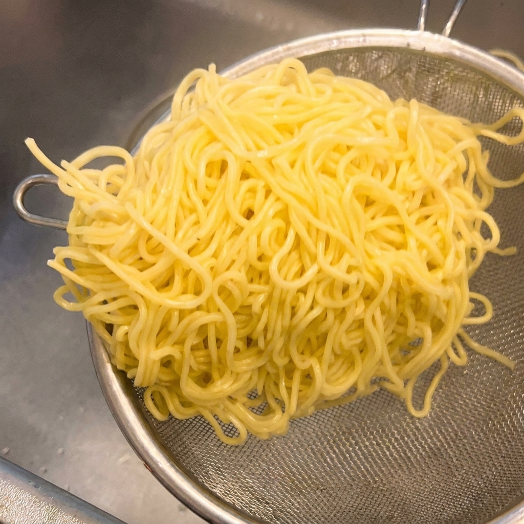 Noodle gialli cotti in un colino a rete metallica scossi con decisione per rimuovere lacqua in eccesso.