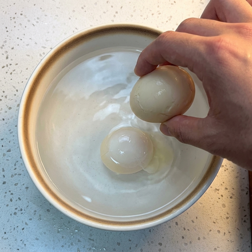 Uovo cotto immerso in una ciotola di ceramica bianca riempita di acqua fredda e cubetti di ghiaccio.