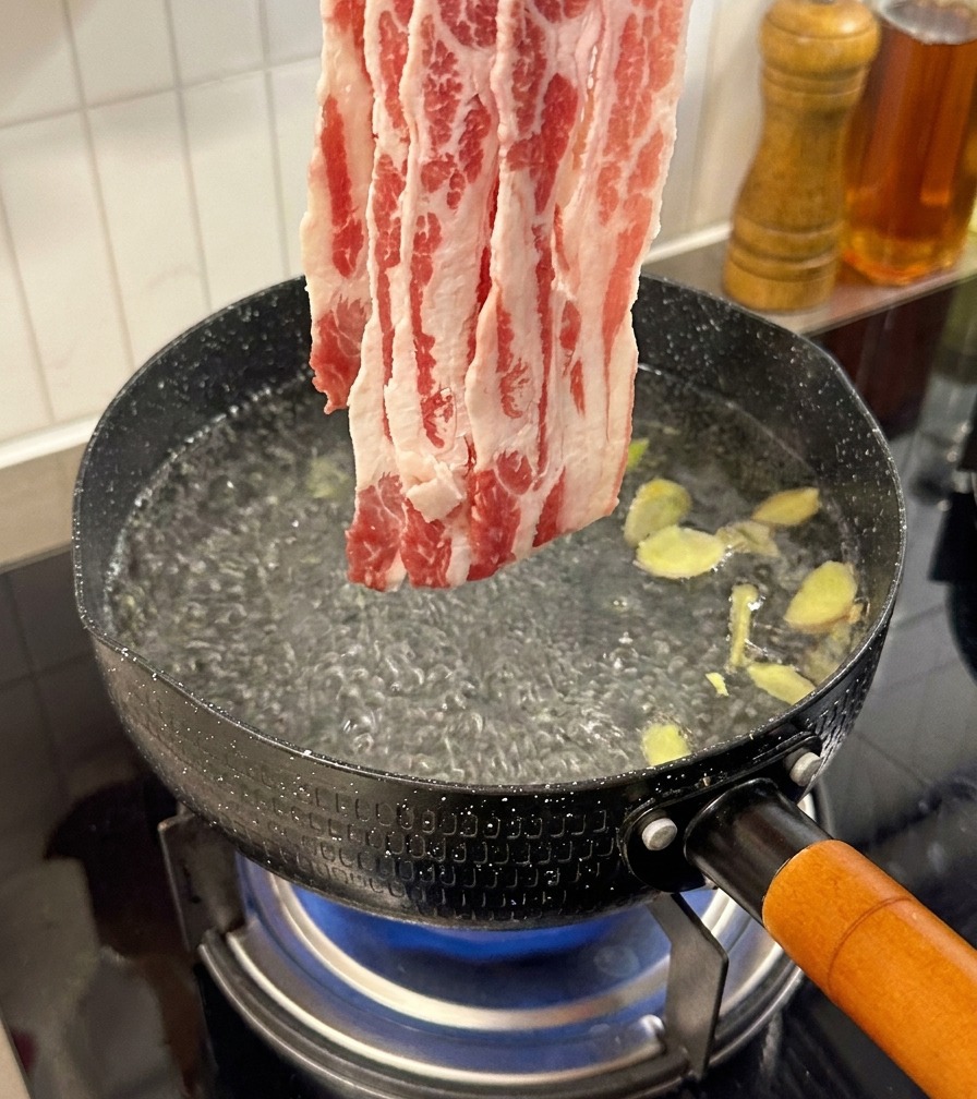 Fettine sottili di manzo crudo aggiunte in acqua bollente con fette di zenzero.