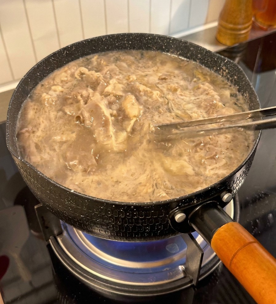 Fettine di manzo sollevate dallacqua bollente con delle pinze.