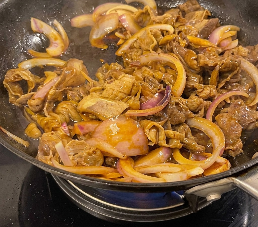Manzo teriyaki e cipolle che sobbollono in una salsa scura e lucida allinterno di un wok.