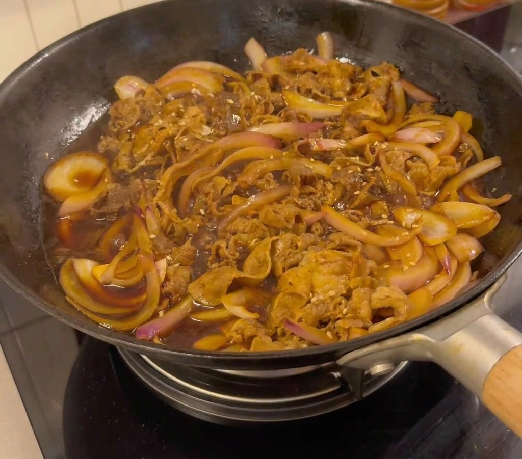 Manzo teriyaki pronto in padella guarnito con semi di sesamo e cipollotti.