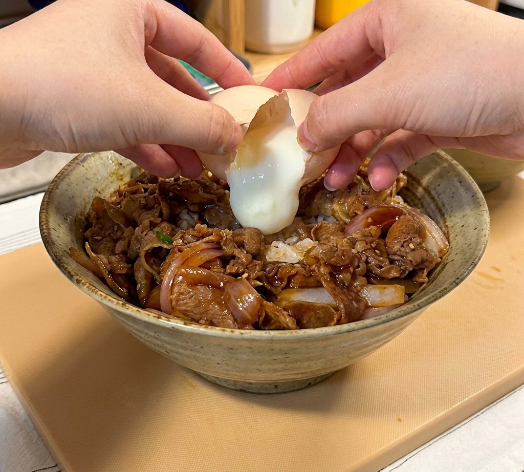 Mani che rompono un uovo onsen sopra la ciotola di riso e manzo.