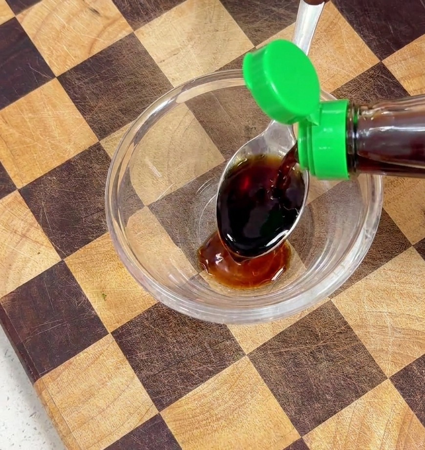 Condimento liquido scuro versato in una ciotola di vetro con salsa di soia.