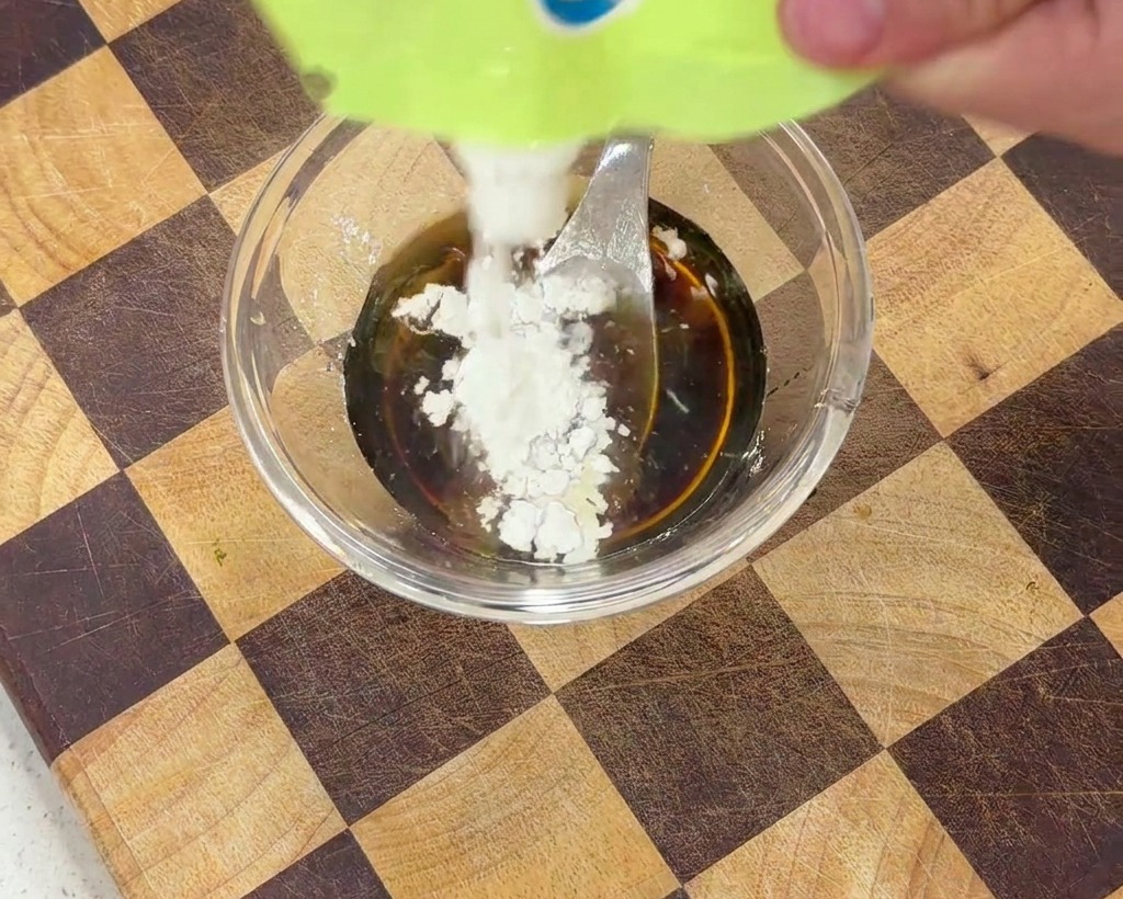 Fecola di mais bianca aggiunta alla salsa scura in una ciotola trasparente.