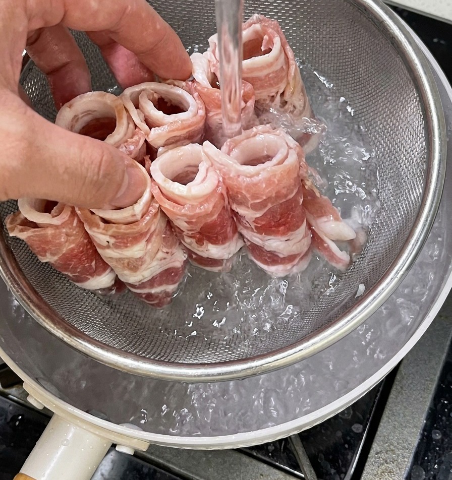 Mano che immerge un colino metallico con fettine di manzo in una pentola dacqua bollente.